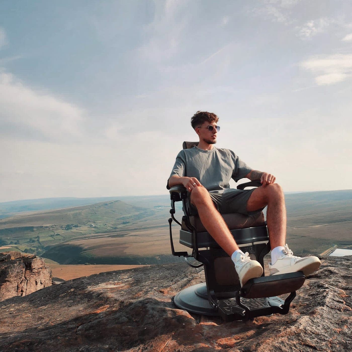 Krystian sitting in a barber's chair on a clifftop, looking out over open moorland.