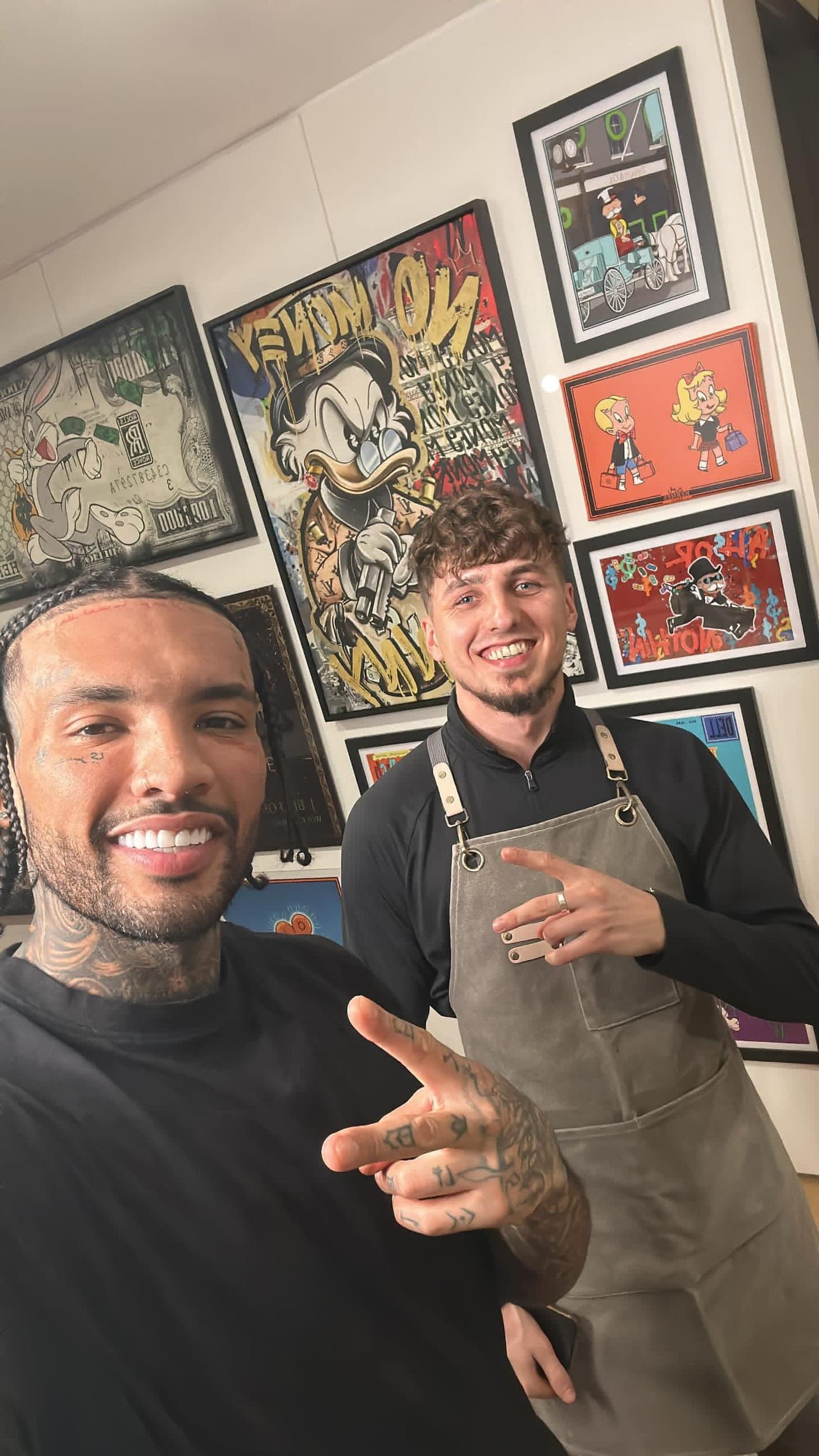 Krystian and a client, Callum Alexandre, smiling after a cut, in front of a wall of framed pop-art prints.
